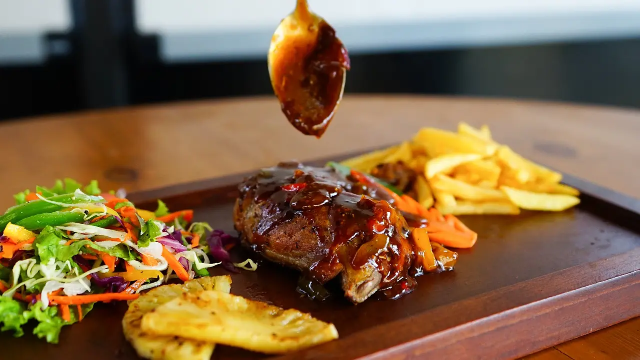 Grilled BBQ chicken leg glazed with sauce, served with French fries, grilled pineapple and side salad